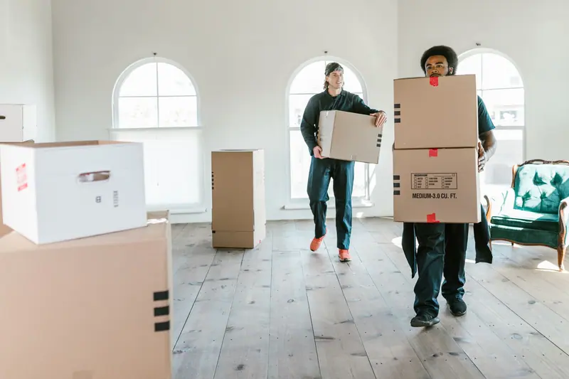 Umzugshelfer tragen Kartons durch eine helle Wohnung